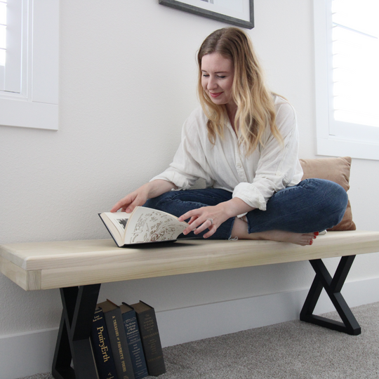 Woman reading a book on a wooden bench in a bright room.