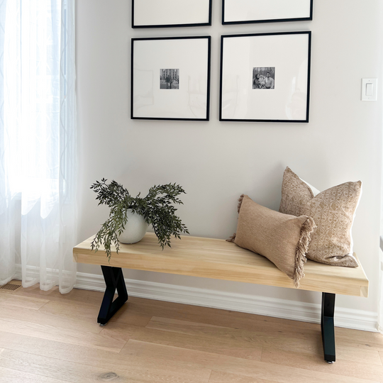 Wooden bench with pillows and a plant against a wall with framed pictures