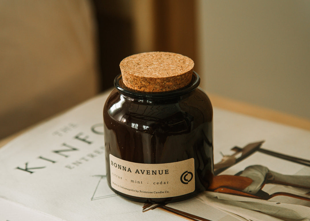 A photo of Primrose Bonna Avenue custom candle on a book next to a bed.  