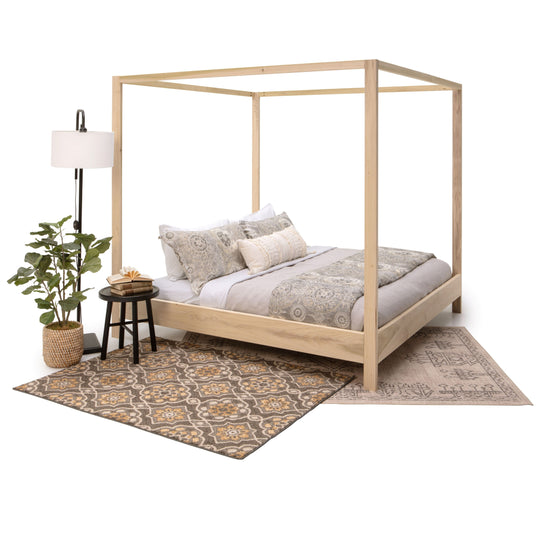 Wooden canopy bed with bedding, side table, and lamp on a patterned rug.