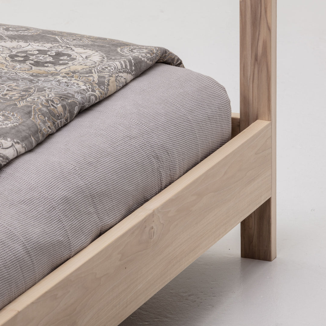 Wooden bed frame with a gray mattress and patterned blanket on a white background
