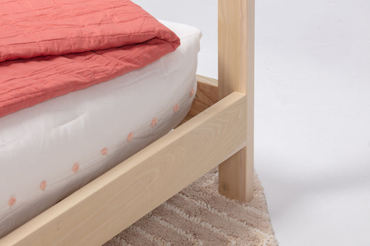 Wooden bed frame with a pink quilt and white mattress on a plain background