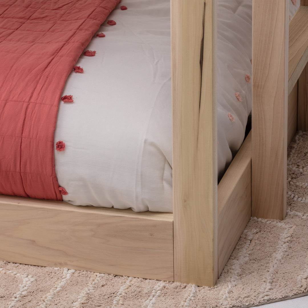 Wooden bed frame with a red textured blanket and white pillow on a beige carpet.