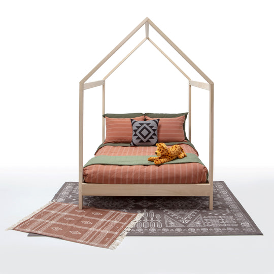 House-shaped bed with bedding and a toy on a patterned rug