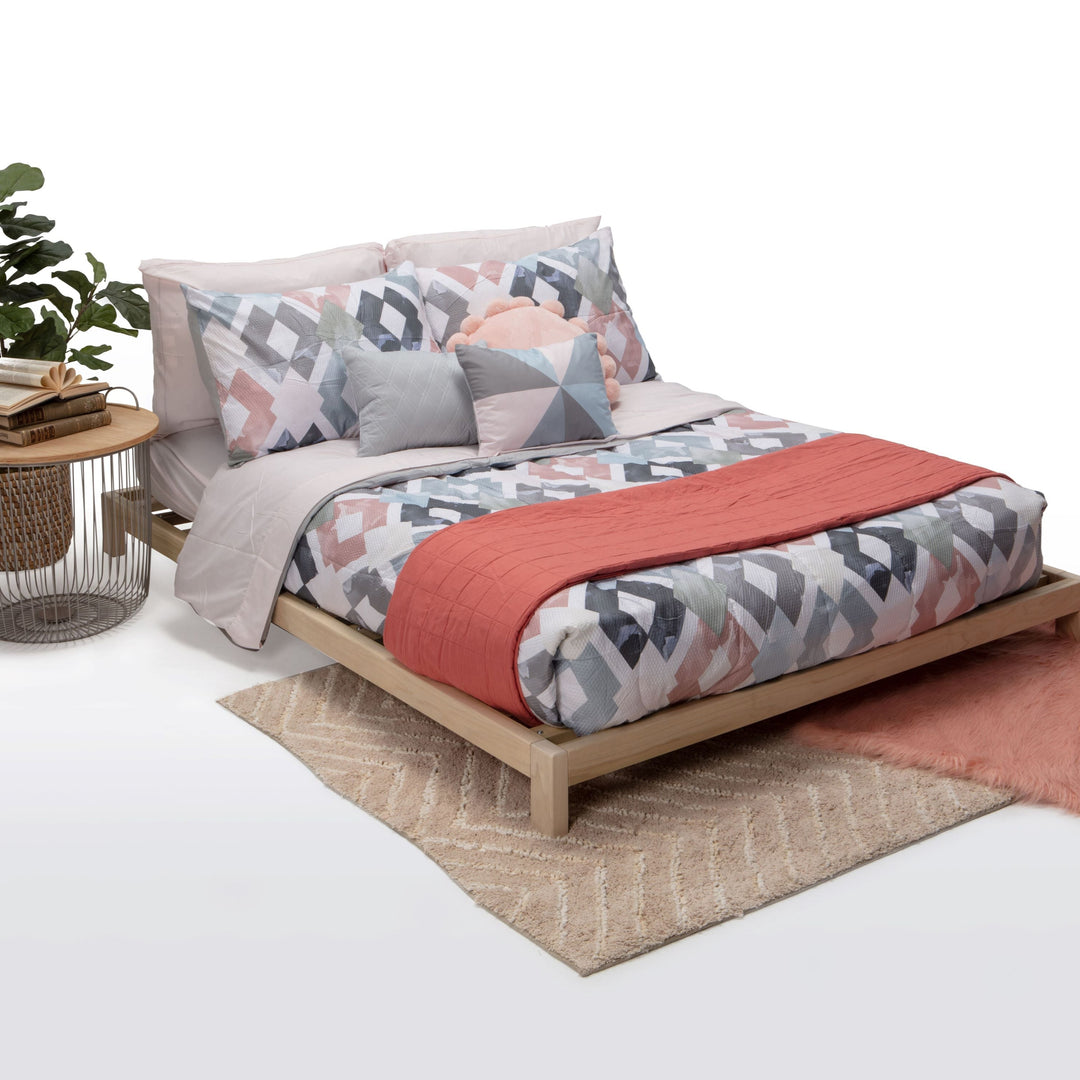 Bed with floral bedding and coral throw on a white background