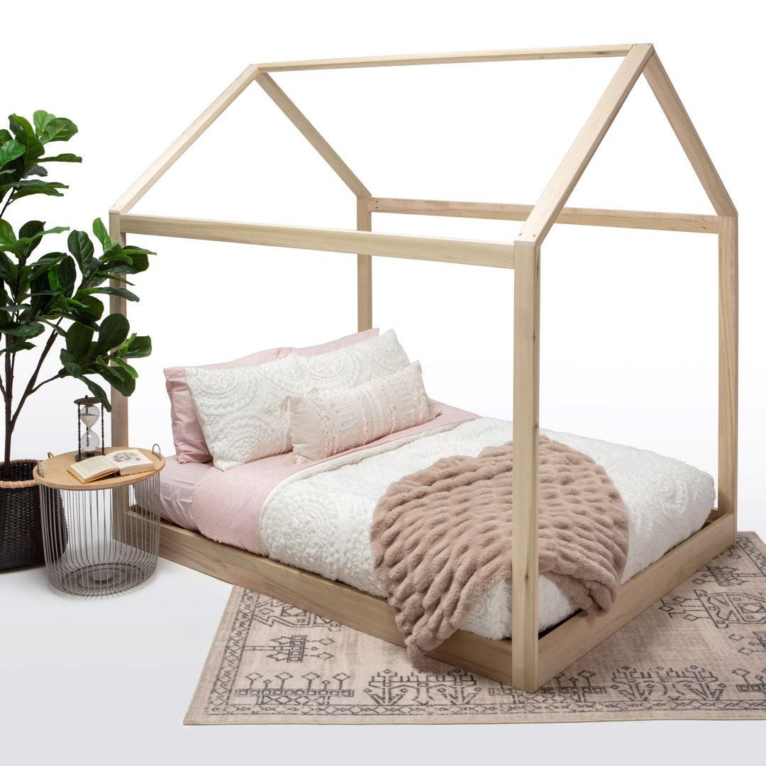 Wooden children's bed with pink bedding and a plant on a white background