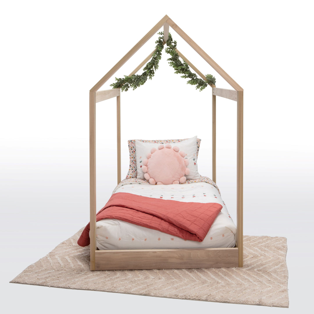 Wooden children's bed with pink bedding and decorative pillows on a white background