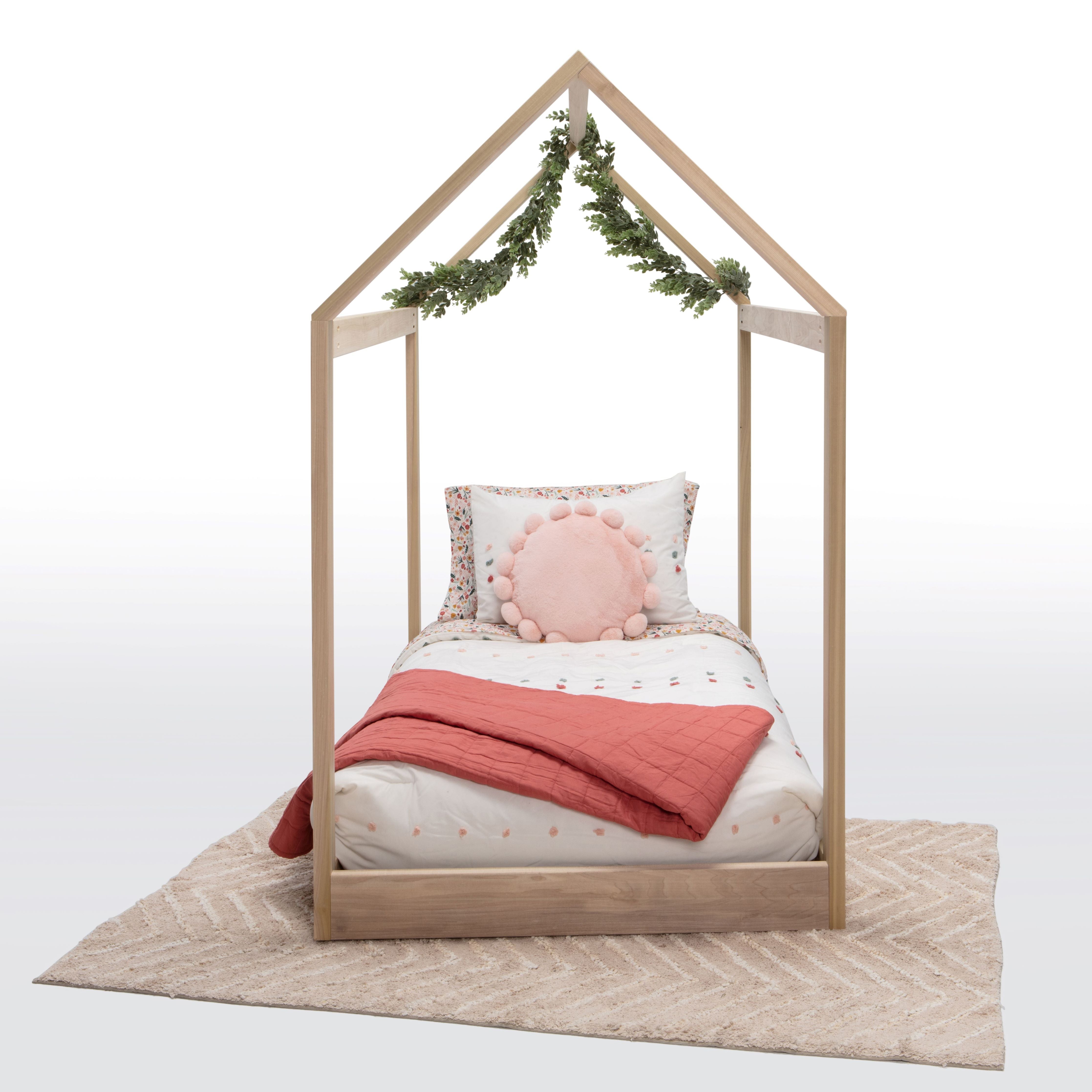 Wooden children's bed with pink bedding and decorative pillows on a white background