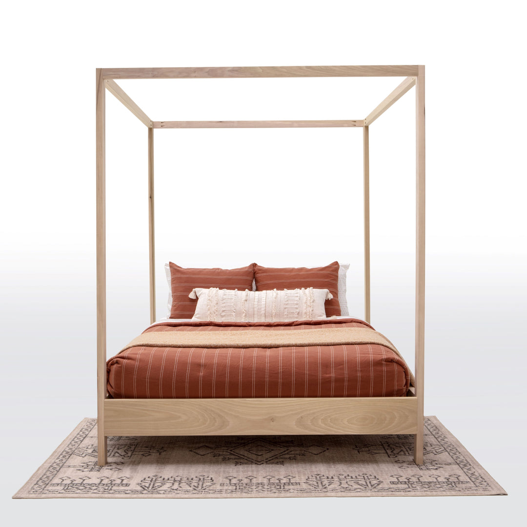 Wooden canopy bed with red bedding and pillows on a white background
