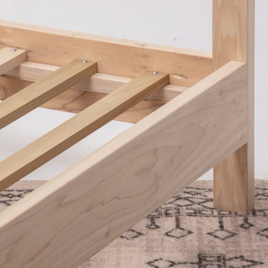 Wooden bed frame on a patterned rug with a white wall background