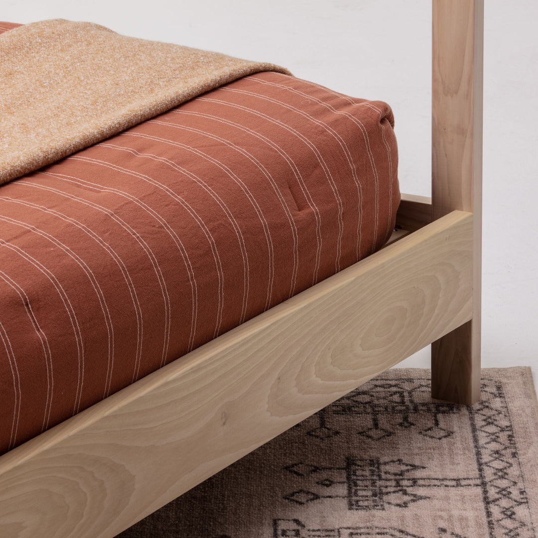 Wooden bed frame with striped bedding and a blanket on a white background
