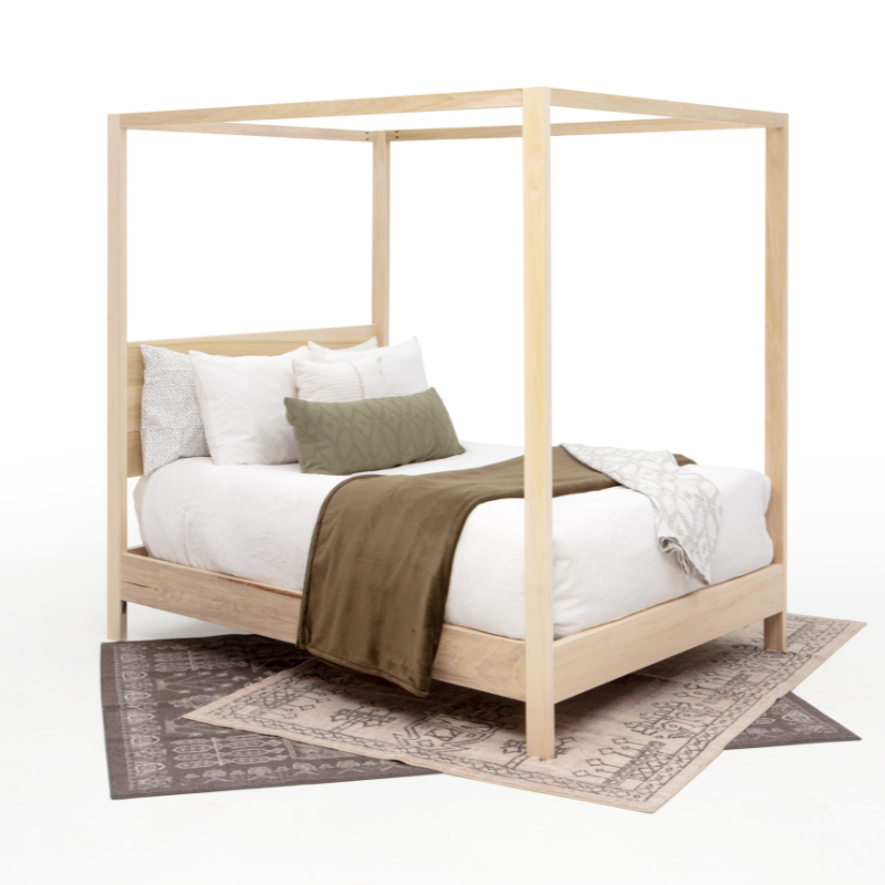 Wooden canopy bed with white bedding and a green blanket on a white background