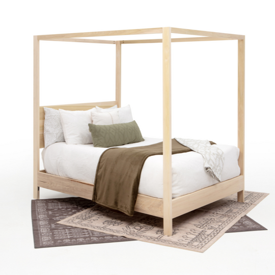 Wooden canopy bed with white bedding and a green blanket on a white background