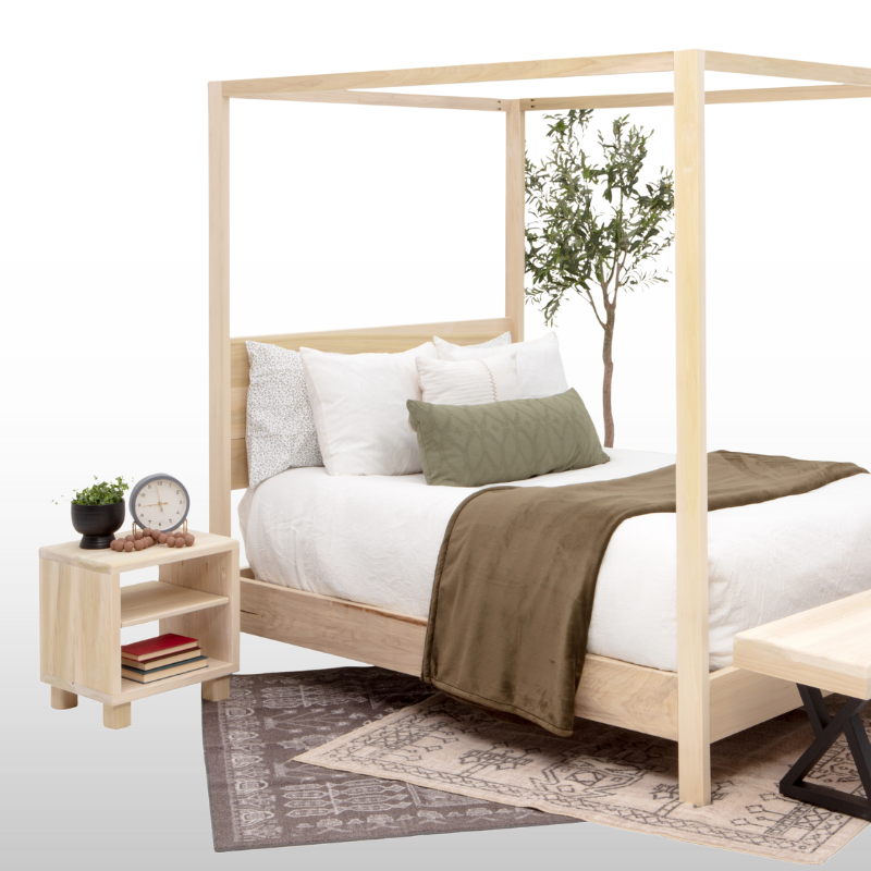 Wooden canopy bed with white bedding and a green throw blanket, nightstand with books and a clock, and small plant.