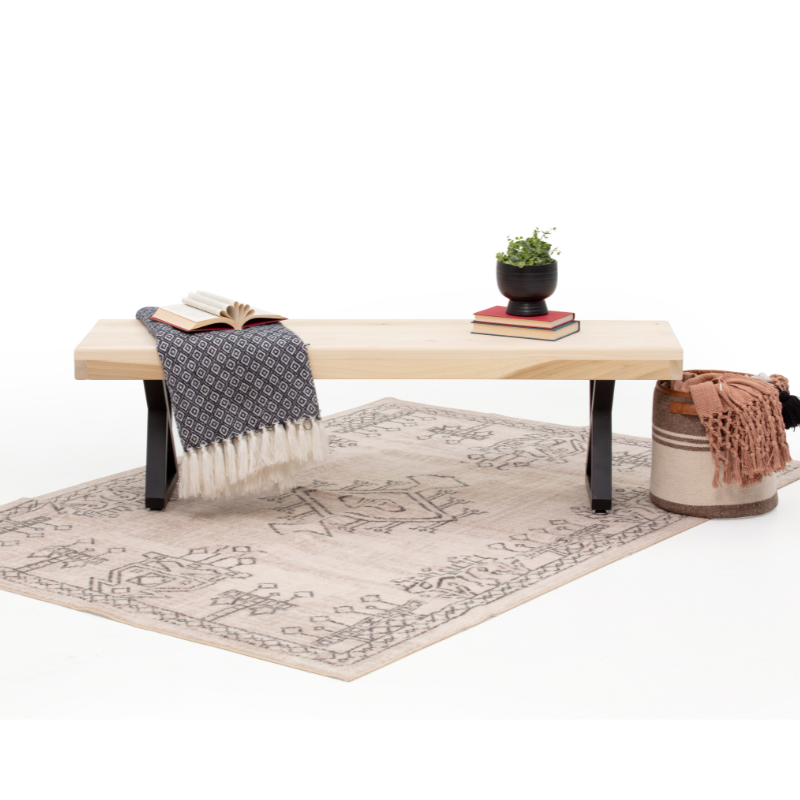 Wooden bench with a blanket, books, and a plant on a patterned rug.