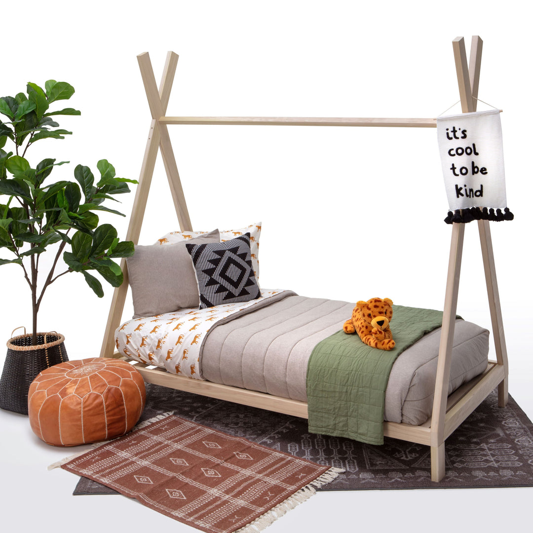 Children's teepee bed with bedding, a plant, and a pouf on a white background